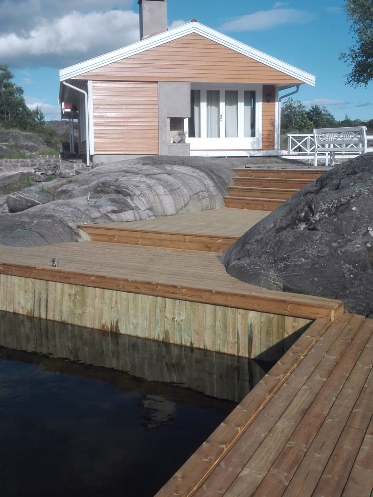 Trebrygge og trapper i tre opp til hytte på svaberg
